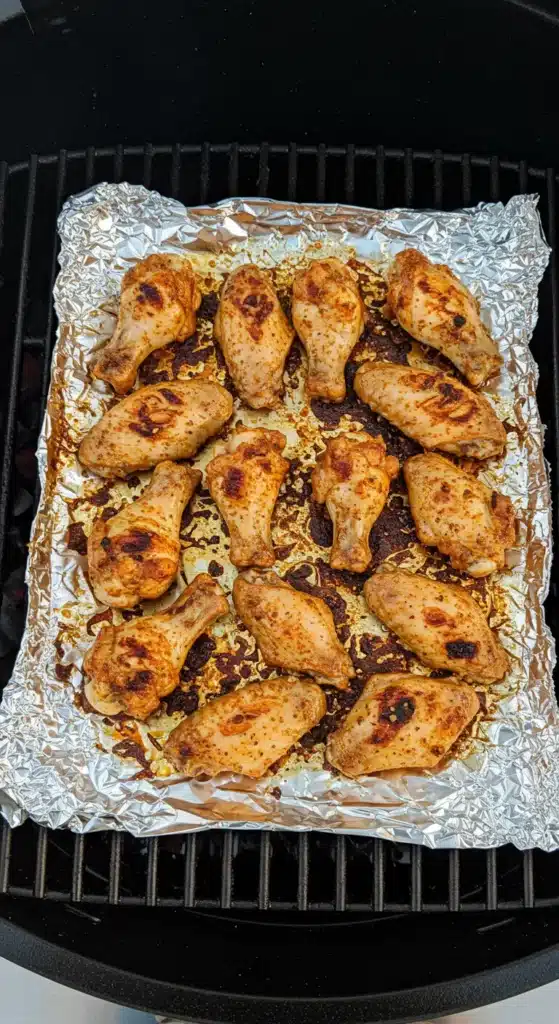Rows of seasoned chicken wings grilling directly on hot grates with light sear marks.