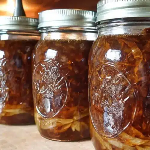 Four quart jars of homemade French onion soup, filled with caramelized onions and rich brown broth, sealed with metal lids and cooling on a wooden counter.