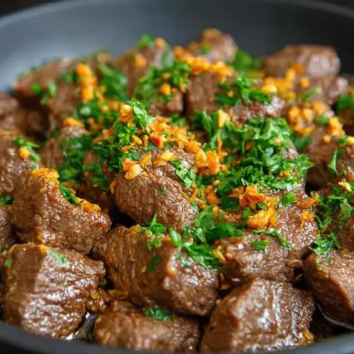 Skillet of beef salpicao—tender seared beef cubes in glossy garlic butter-soy sauce, sprinkled with chopped parsley.