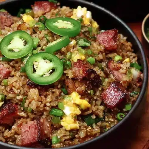 Bowl of brisket fried rice with crispy smoked brisket pieces, scrambled egg, scallions, and jalapeño slices, served with dipping sauce and chopsticks.