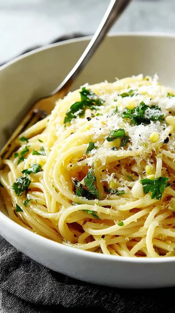 Bowl of lemon garlic spaghetti topped with fresh parsley and grated Parmesan, served warm with a fork.