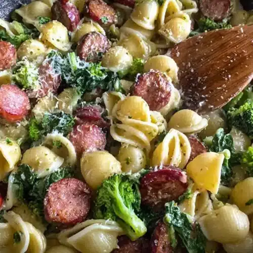Creamy shell pasta with smoked sausage slices and tender broccoli florets in a skillet.