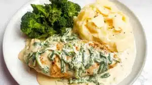 Seared chicken breast smothered in a rich Boursin garlic-herb cream sauce with wilted spinach, served on a white plate alongside mashed potatoes and steamed broccoli.