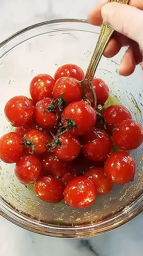 Easy Cherry Tomatoes Recipes: Roasted to Perfection 3 hand stirring cherry tomatoes in a glass bowl with olive oil, garlic, and herbs before roasting