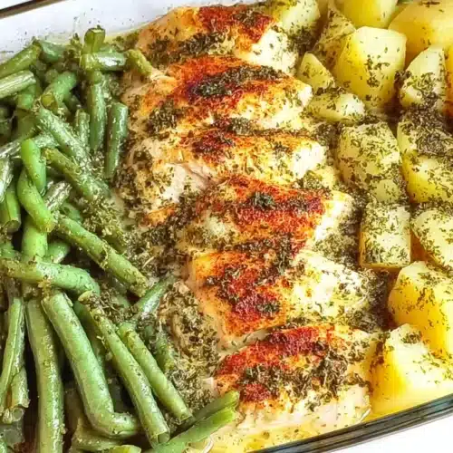 Glass baking dish with herb-seasoned chicken breasts, diced potatoes, and green beans baked together in a buttery broth.