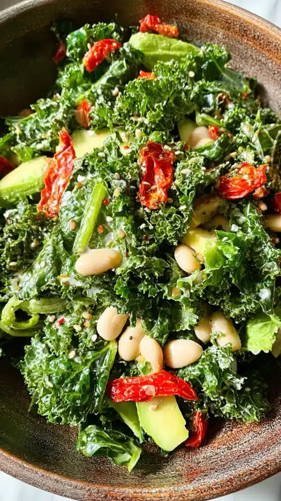 Close-up of kale leaves coated in creamy dressing with white beans and sun-dried tomatoes scattered throughout.