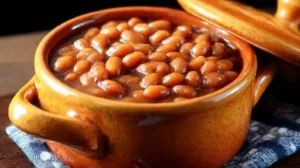 Easy low sodium baked beans served in a rustic brown crock, beans glistening in thick sauce on a blue patterned napkin.