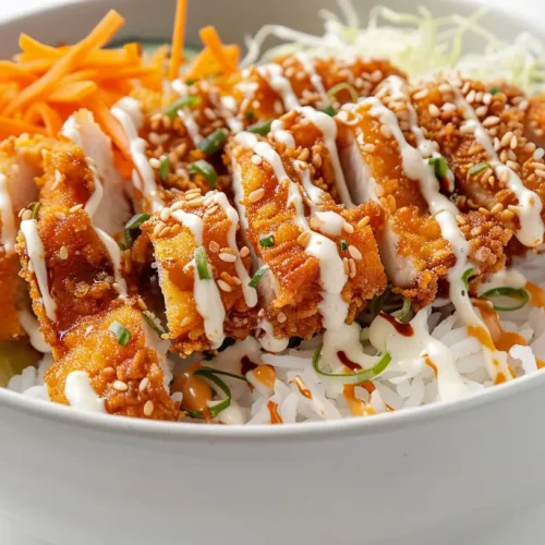Crunchy chicken rice bowl with crispy breaded chicken, carrots, cucumber, and creamy sauce over white rice.