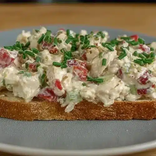 Side view of an open-faced easy chicken salad no celery sandwich on rustic bread, garnished with chopped chives.