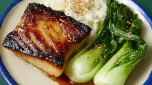 glazed miso black cod fillet with caramelized edges served beside steamed rice and sautéed baby bok choy on a plate