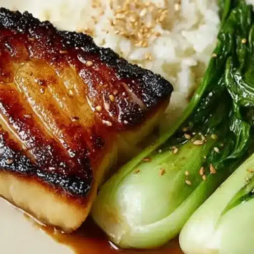 glazed miso black cod fillet with caramelized edges served beside steamed rice and sautéed baby bok choy on a plate