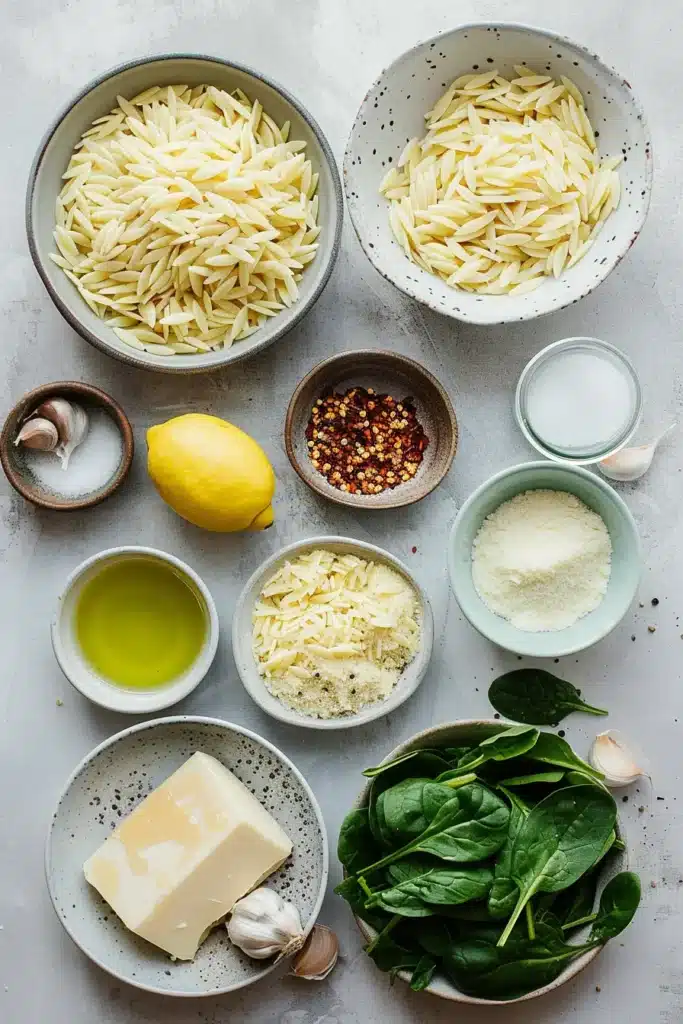 Overhead view of bowls with orzo, spinach, butter, olive oil, garlic, lemon, cheeses, red pepper flakes, and salt.
