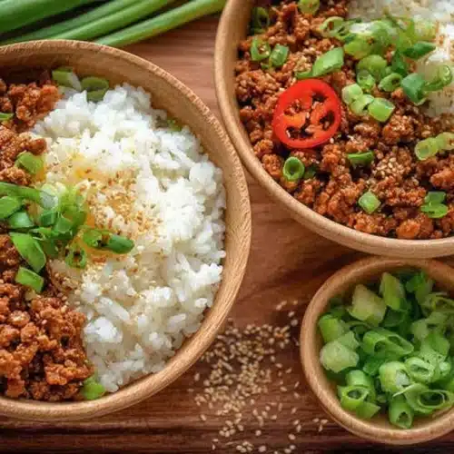 Two wooden bowls with ground turkey and rice, topped with scallions and sesame seeds