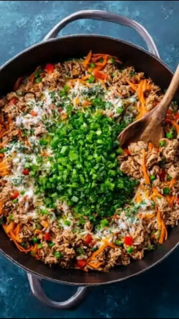 Ground turkey and vegetables in a large skillet with chopped scallions and creamy sauce pooled in the center