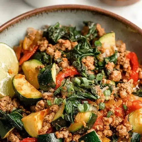 Bowl of ground turkey and zucchini skillet topped with scallions and lime