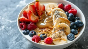 Top view of a protein pancake bowl with mini pancakes, yogurt, banana slices, strawberries, raspberries, blueberries and peanut butter drizzle.
