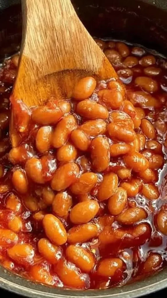 Low sodium baked beans simmering in a rich tomato sauce, wooden spoon scooping up tender beans.