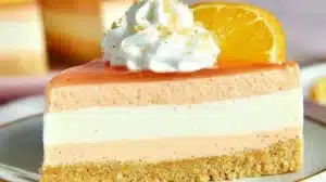 Orange Cream Cheesecake Recipe: Easy No-Bake Layers Slice of no-bake orange cream cheesecake with three creamy layers, graham cracker crust, whipped cream, and an orange slice on top.
