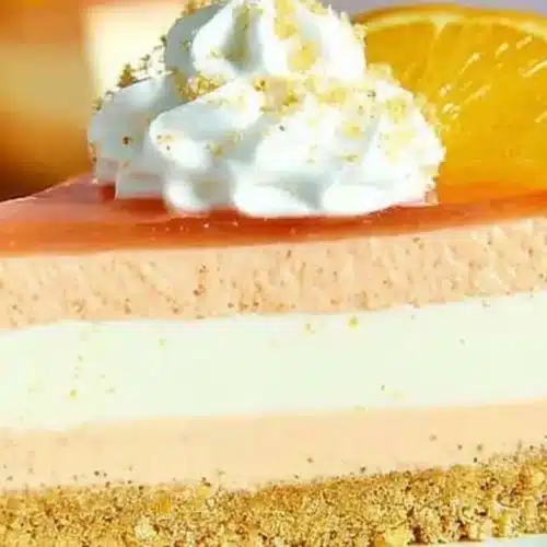 Orange Cream Cheesecake Recipe: Easy No-Bake Layers 5 Slice of no-bake orange cream cheesecake with three creamy layers, graham cracker crust, whipped cream, and an orange slice on top.