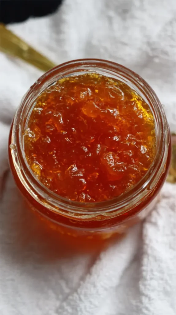 Open glass jar filled with bright orange marmalade on a white towel.