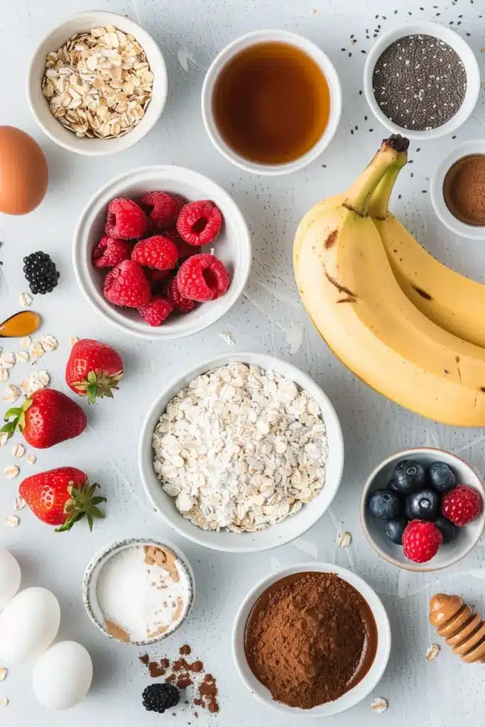 Overhead view of ingredients for a protein pancake bowl including oats, bananas, berries, eggs, chia seeds and honey.