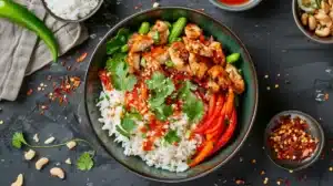 Overhead sweet chili chicken rice bowl with bell peppers, cilantro and spicy sauce drizzled over white rice.