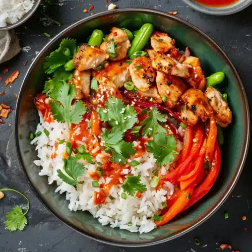 Overhead sweet chili chicken rice bowl with bell peppers, cilantro and spicy sauce drizzled over white rice.
