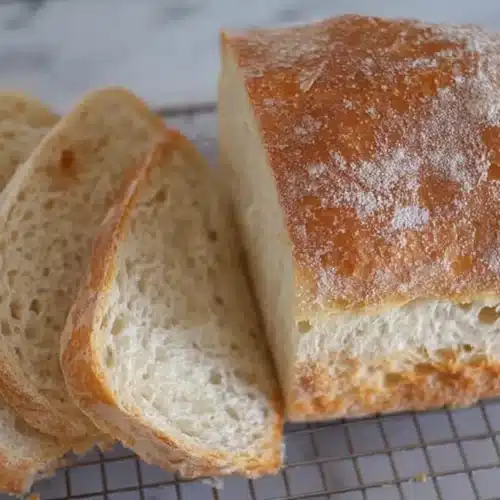 Golden-crusted potato-flake sourdough loaf, partially sliced on a wire rack, showing an airy, tender crumb.
