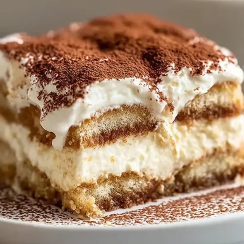 The Best Tiramisu Recipe served as a creamy layered slice with espresso-soaked ladyfingers and a cocoa-dusted top on a white plate