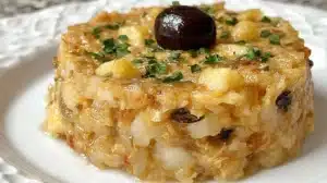 Round Bacalhau à Brás recipe on a white plate, topped with one black olive and sprinkled with chopped parsley.