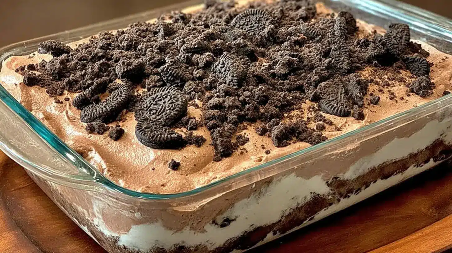 Layered Dirt Cake Recipe in a glass pan showing creamy chocolate layers, cookie crust, and crushed cookies scattered over the top