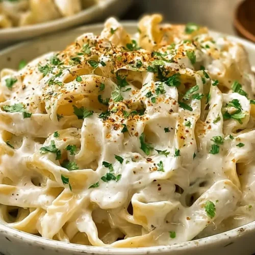 High Protein Alfredo Sauce over pasta in a light bowl, garnished with parsley and black pepper
