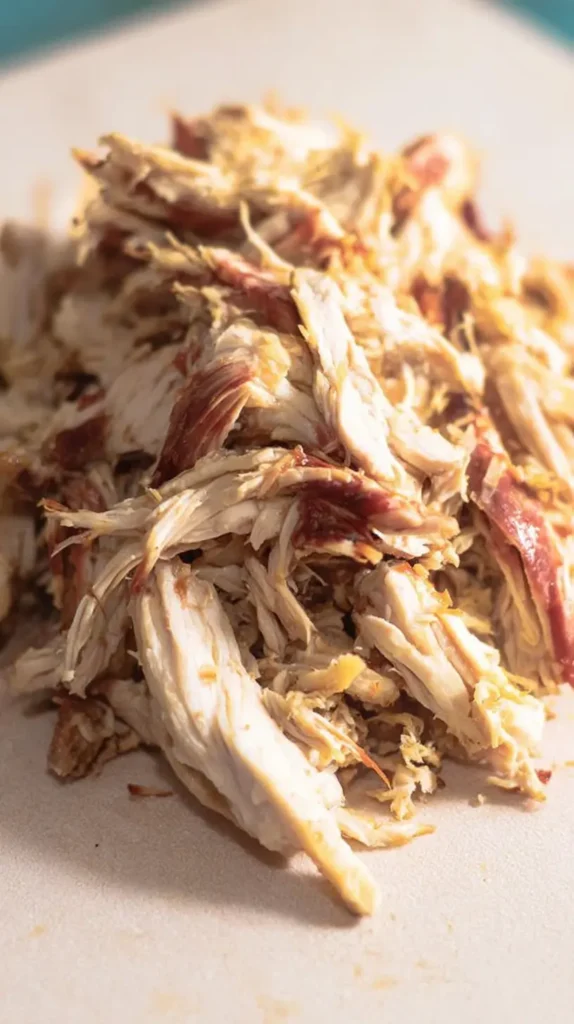 Close-up of juicy shredded chicken piled on a cutting board, ready to be added to a light Hawaiian chicken long rice recipe.