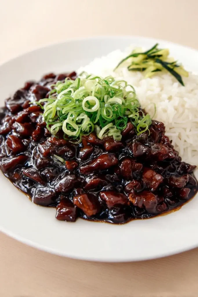 Jajangmyeon served with glossy Korean black bean sauce, diced pork, sliced green onions, and steamed white rice on a white plate