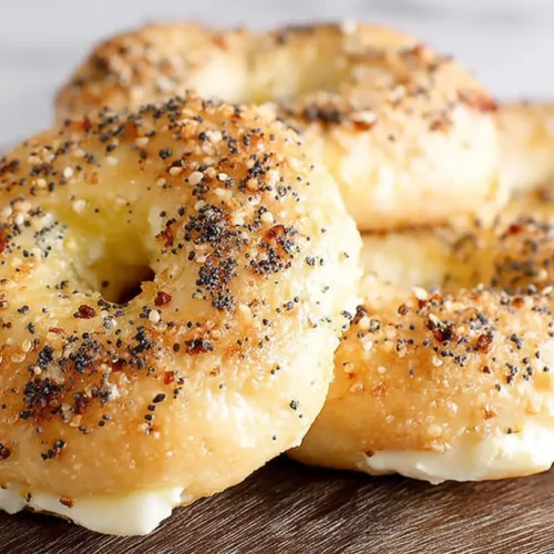 Close-up of golden cottage cheese bagels topped with everything seasoning on a wooden board.