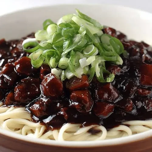 Jajangmyeon Korean black bean noodles topped with diced pork, onion sauce, and fresh sliced green onions in a white bowl