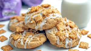 Cinnamon Toast Crunch Cookies stacked on a plate with vanilla glaze drizzle and Cinnamon Toast Crunch cereal pieces scattered around