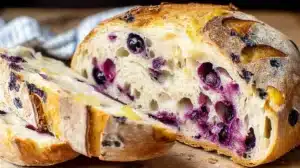 Sliced lemon blueberry sourdough bread on a wooden board, showing a crusty golden crust and airy crumb studded with blueberries.