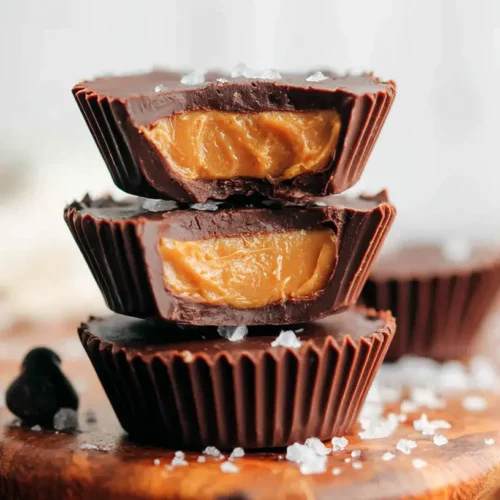 Peanut Butter Cups stacked on a wooden board with flaky sea salt and chocolate chips around them