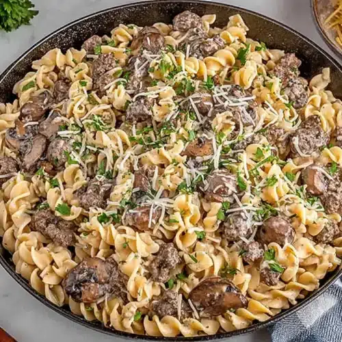 Ground Beef Stroganoff cooked in a skillet with egg noodles, mushrooms, creamy sauce, and a shower of parsley and shredded cheese