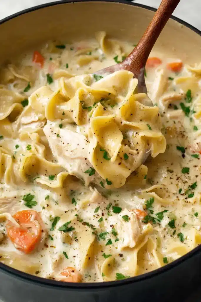 Creamy Chicken Noodle Soup being scooped with a ladle showing egg noodles, chicken, carrots, and creamy broth with herbs