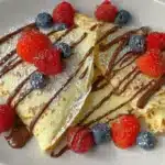 Quick and easy crepes served on a plate with chocolate drizzle, mixed berries, and powdered sugar