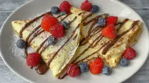Quick and Easy Crepe Recipe: Proven, Tender and Thin Quick and easy crepes served on a plate with chocolate drizzle, mixed berries, and powdered sugar