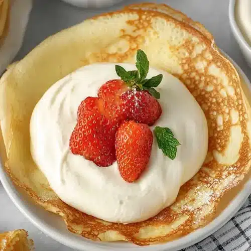 Cream Cheese Crepe Filling: Easy, Light, Flavor-Packed 2 Cream Cheese Crepe Filling piled in a golden crepe and topped with fresh strawberries and mint on a light gray surface