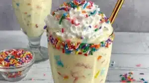 Birthday cake protein milkshake with colorful sprinkles and whipped cream.