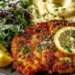 Crispy Chicken Milanese served with lemon and greens on a white plate