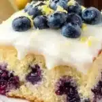A slice of moist Lemon Blueberry Cake topped with fresh blueberries and lemon zest.