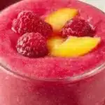 A refreshing Raspberry Peach Smoothie garnished with fresh raspberries and peaches.