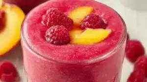 A refreshing Raspberry Peach Smoothie garnished with fresh raspberries and peaches.
