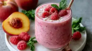 Delicious Raspberry Peach Smoothie in a glass garnished with fresh fruit.